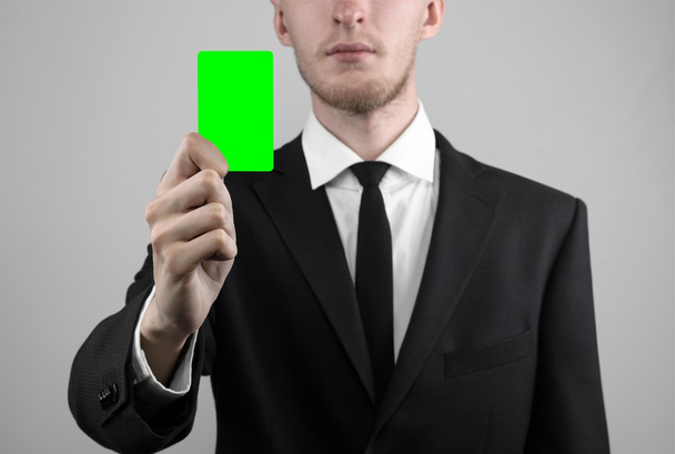 üzletember egy fekete színű és fekete nyakkendő gazdaság egy, a kezében egy kártya, a zöld kártya, a kártya behelyezésre, a zöld chroma key-card, szürke háttér, elszigetelt, üzleti téma, téma, a banki - Fotó, kép