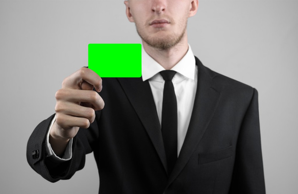 zakenman in een zwart pak en zwarte stropdas bedrijf een kaart, een hand met een kaart, groene kaart, kaart is geplaatst, de groene chroma key-card, grijze achtergrond, geïsoleerde, zakelijke thema, thema van het bankwezen - Foto, afbeelding