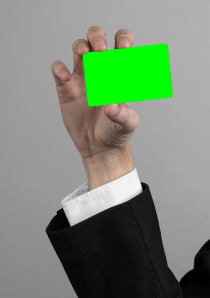 podnikatel v černé a černou kravatu hospodářství, které je vložena karta, ruka drží kartu, Zelená karta, karta, kódovanou kartu zelené barvy, šedé pozadí, izolované, obchodní téma, téma bankovnictvi - Fotografie, Obrázek