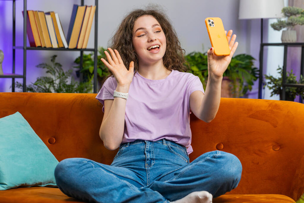 Portrait of young woman making phone call conversation with friends sitting on sofa. Happy excited girl enjoying mobile smartphone loudspeaker talking indoors at modern home living room apartment - Foto, Imagem