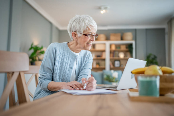 Старшая белая женщина использует ноутбук дома для работы - Фото, изображение