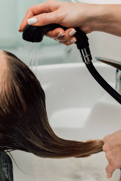 Um cabeleireiro lava um cabelo loiro em um salão de beleza. Cuidados com o cabelo e tratamento. Foto de alta qualidade - Foto, Imagem