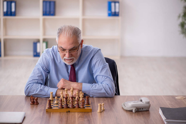 Stary męski pracownik gra w szachy w biurze - Zdjęcie, obraz