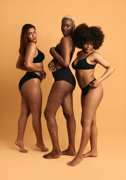 Full body of multiracial female models in black lingerie showing body difference on brown background - Fotografie, Obrázek