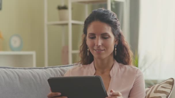 Atraktivní brunetka žena sedí uvolněně na gauči v moderním obývacím pokoji pomocí digitálního tabletu - Záběry, video