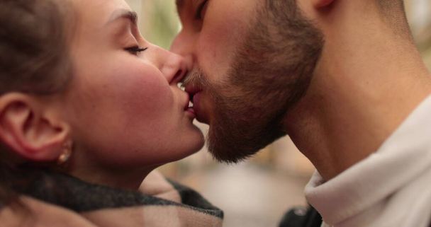 Primer plano de las caras de una joven pareja enamorada besándose y abrazándose en la calle en un sombrío día de otoño. - Foto, Imagen