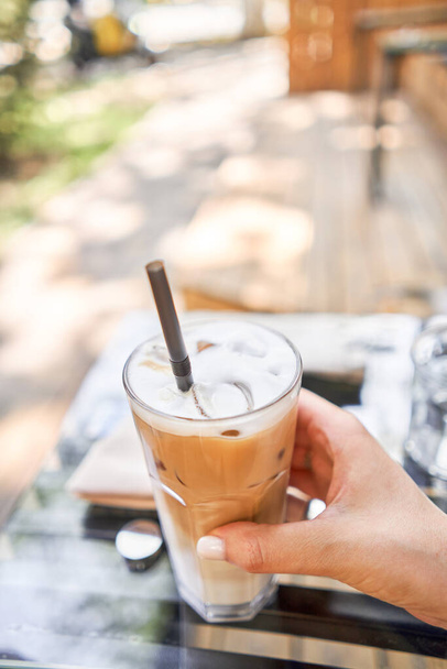 Ein Glas kalten Cappuccino mit Eis. Der Tisch im Coworking Space des Coffeeshops. Eine Tasse Kaffee auf der Veranda an einem sonnigen Tag. Kaffeepause im Café. Nahaufnahme. Hochwertiges Foto. - Foto, Bild