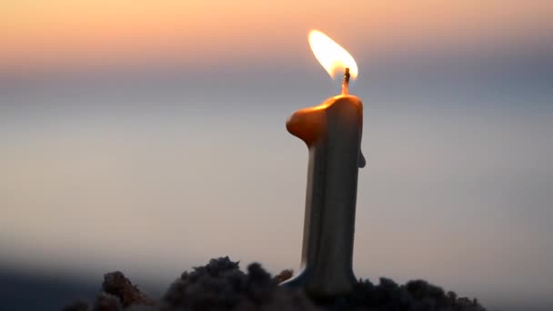 Płonący parafinowy świeca w kształcie liczba 1 Jeden w piasek na plaża morski brzeg w pobliżu woda morski fala przy zachód słońca świt zbliżenie. Koncepcja wakacje Urodziny Nowy Rok świętowanie romantyczne wakacje - Materiał filmowy, wideo