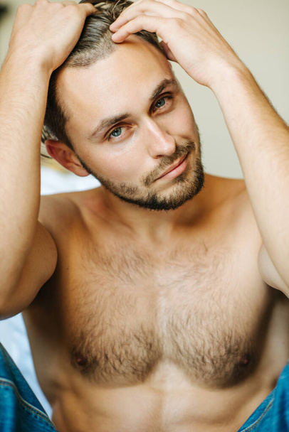 Uzun saçlı ve açık renk sakallı yakışıklı bir adamın yakın portresi. Seksi fitness elemanı kameraya bakıyor. Otel odasında poz veren sakallı erkek model.. - Fotoğraf, Görsel