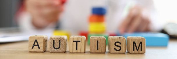 Word autism on wooden blocks close-up and blurred doctor with multi-colored blocks and toys in background. Autism treatment concept. - Foto, imagen