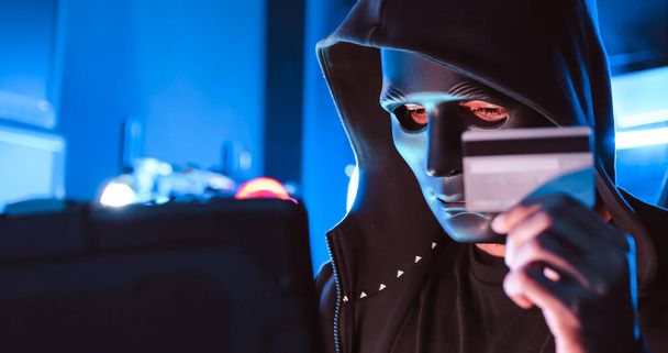Haker w masce zakrywającej twarz używa komputera do zhakowania danych, by zdobyć okup od ofiar.. - Zdjęcie, obraz