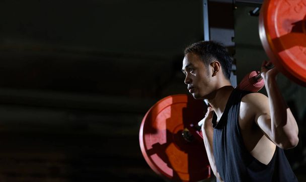 Ázsiai izmos sport ember gyakorolja súly képzés halálos felvonó súlyzó a magizom belsejében tornaterem sötét háttér gyakorlása és edzés  - Fotó, kép