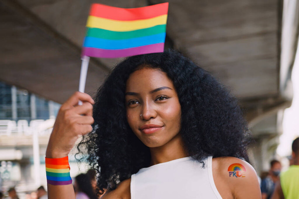 Una joven mujer negra con pegatinas de tatuajes de arco iris y mostrando símbolos de homosexualidad en desfile de orgullo. - Foto, Imagen
