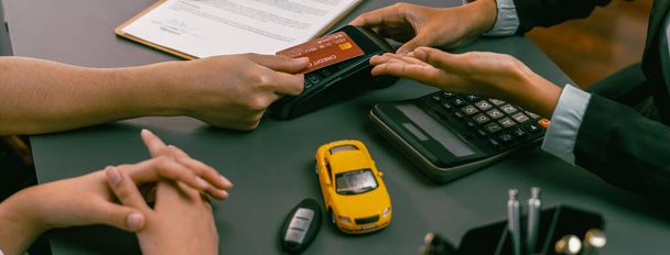 Klient kupuje nowy samochód z kartą kredytową za pośrednictwem terminalu elektronicznego po zakończeniu transakcji z dealerem samochodowym. Płynny transfer własności samochodu z bezpieczną elektroniczną płatnością cyfrową. Cudowne dziecko - Zdjęcie, obraz