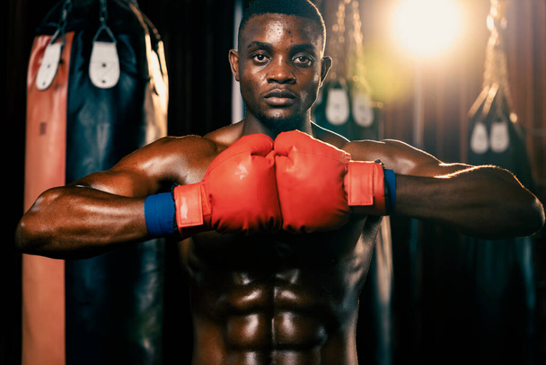 Bojovník v boxu pózuje, Afroameričan Black boxer dal ruku nebo pěst v rukavici k sobě v agresivním postoji a připraven k boji v tělocvičně s kopací taškou a boxerskou výstrojí. Impetus - Fotografie, Obrázek