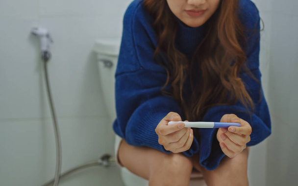 トイレに座って妊娠検査結果を待っているストレスのない女性. - 写真・画像