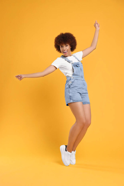 Happy young woman dancing on orange background - Valokuva, kuva