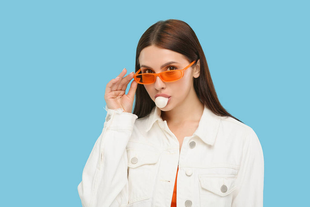 Beautiful woman in sunglasses blowing bubble gum on light blue background - Foto, immagini