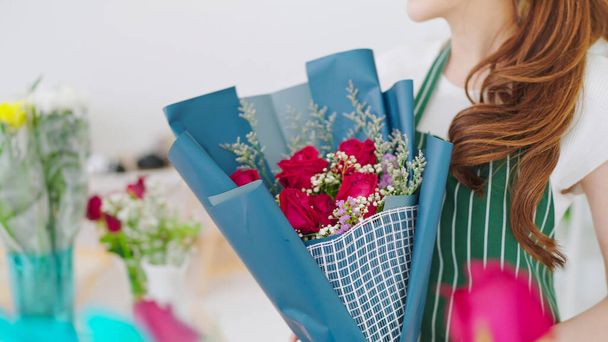 Jovem mulher asiática florista em avental passando buquê para cliente mulher na loja de flores. Close up buquê de rosa flor a mãos - Foto, Imagem