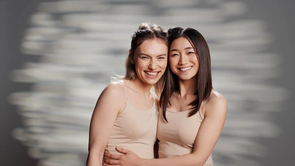 Interracial girls smiling and feeling confident on camera, posing for beauty ad campaign. Cheerful flawless women promoting body positivity and self love with skincare routine or products. - Photo, Image