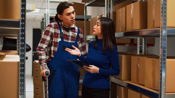Young man walking in crutches with female owner, talking about stock management and inventory. Entrepreneur working with tablet to analyze merchandise, teamwork with employee. - Foto, Imagen
