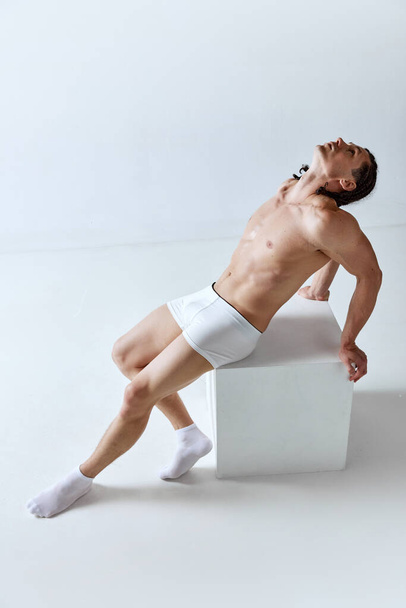 Full-length portrait of muscular handsome man with perfect, fit body shape posing in underwear over grey studio background. Concept of mens beauty, body care, sport, wellness, healthy lifestyle, ad - Φωτογραφία, εικόνα