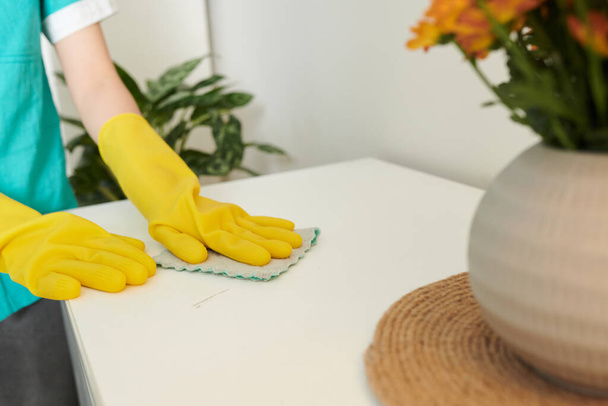 Huisreiniger draagt siliconen handschoenen bij het desinfecteren van high-touch gebieden in huis - Foto, afbeelding