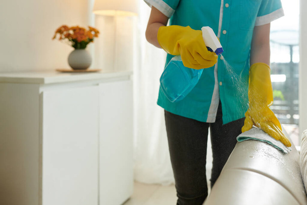 ベージュレザーソファに洗剤を噴霧するシリコーン手袋のハウスクリーナー - 写真・画像