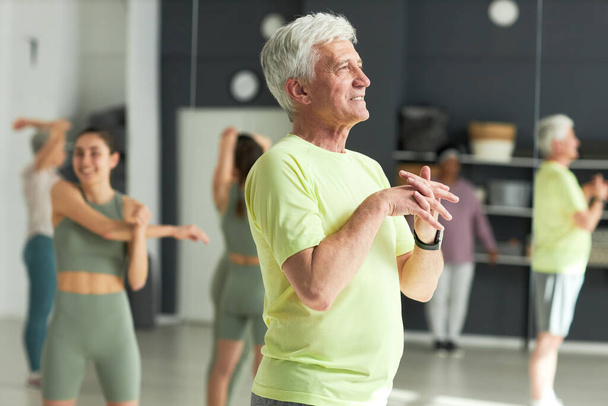 Senior man oefenen in health club met andere mensen op de achtergrond - Foto, afbeelding