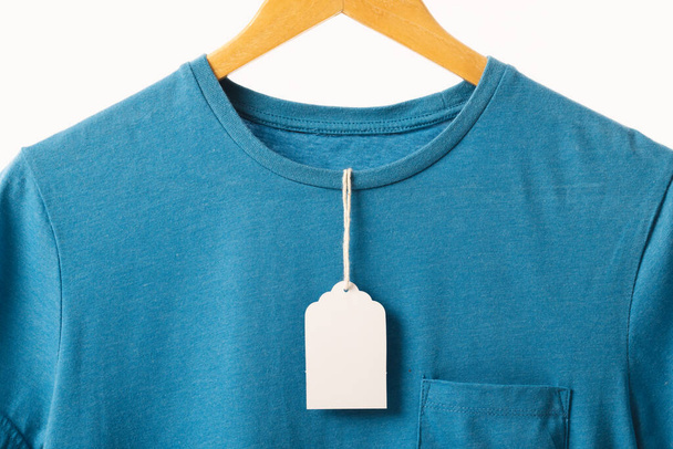 Blue t shirt with tag on hanger with copy space on white background. Fashion, clothes, colour and fabric concept. - Фото, зображення