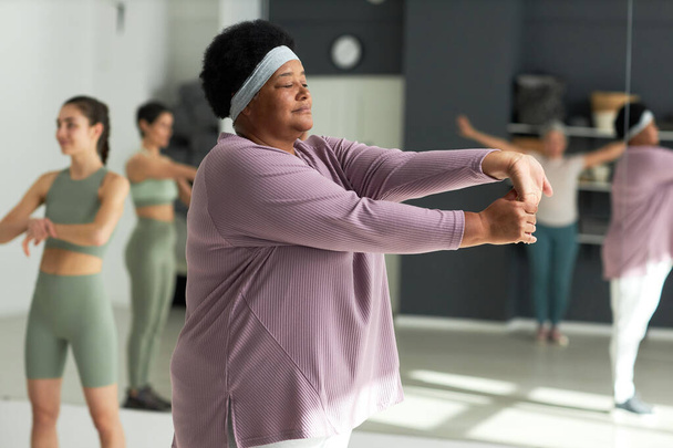 Afroamericana regordeta mujer entrenamiento en gimnasio con otras personas en segundo plano - Foto, imagen