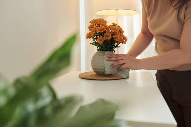 Ausgeschnittenes Bild einer Frau, die mit weichem Tuch Vase auf Eingangstisch wischt - Foto, Bild