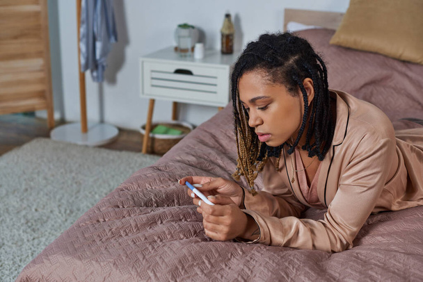mujer afroamericana acostada en la cama, mirando la prueba de embarazo, tomando decisiones, concepto de aborto - Foto, Imagen