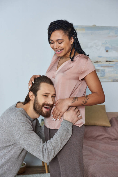 felice uomo che ascolta pancia della moglie africana americana incinta, fertilità, coppia, futuri genitori - Foto, immagini