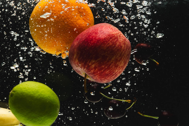 Close up of fresh fruit falling into water with copy space on black background. Fruit, food, freshness and colour concept. - Zdjęcie, obraz