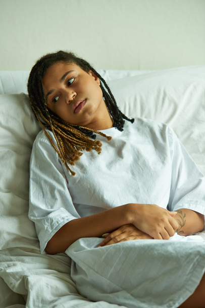 dolor, mujer afroamericana deprimida acostada en una sala privada, hospital, concepto de aborto espontáneo, tatuaje - Foto, Imagen