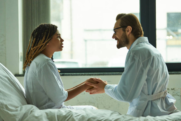 врач утешает африканскую американку, держит за руки пациента, частную палату, больницу, улыбается - Фото, изображение