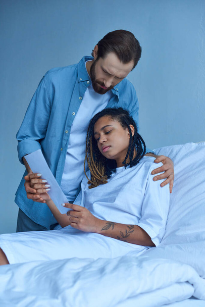 trieste man in de buurt van Afrikaanse Amerikaanse vrouw, kijken naar echografie, ziekenhuis, miskraam concept - Foto, afbeelding