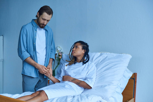 Fehlgeburtenkonzept, Mann hält Hand von depressiver afrikanisch-amerikanischer Frau, Krankenhaus, Privatstation - Foto, Bild