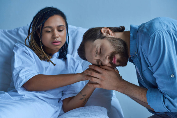 Концепция выкидыша, грустный мужчина скорбит и держит за руки африканскую американскую жену, больничную палату - Фото, изображение