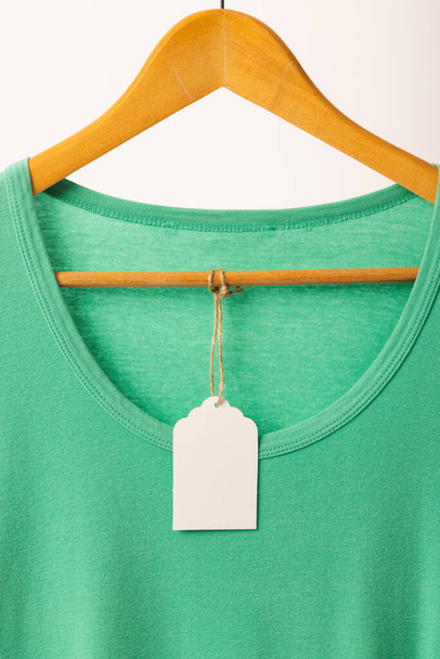 Green t shirt with tag on hanger with copy space on white background. Fashion, clothes, colour and fabric concept. - Фото, зображення