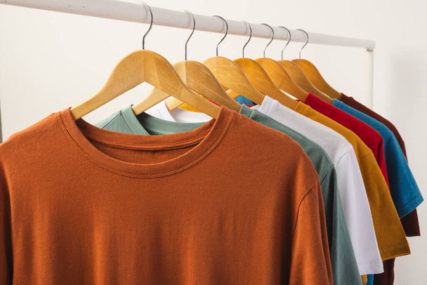 Multi coloured t shirts on hangers hanging from clothes rail and copy space on white background. Fashion, clothes, colour and fabric concept. - Fotografie, Obrázek