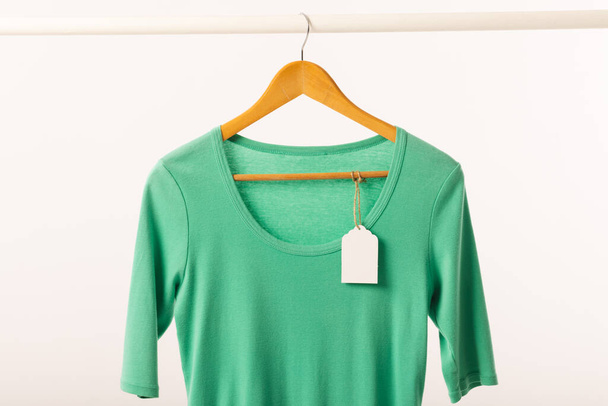 Green t shirt with tag on hanger hanging from clothes rail with copy space on white background. Fashion, clothes, colour and fabric concept. - Foto, Imagem