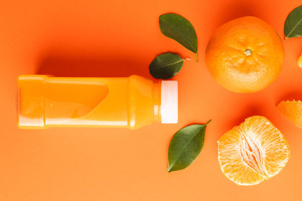 Close up of bottle with juice, tangerine, segments and leaves with copy space on orange background. Fruit, food, freshness and colour concept. - 写真・画像