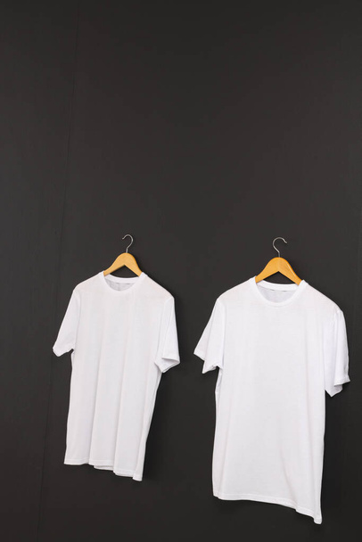 Two white t shirts on hangers and copy space on black background. Fashion, clothes, colour and fabric concept. - Photo, image