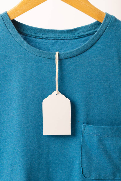Blue t shirt with tag on hanger with copy space on white background. Fashion, clothes, colour and fabric concept. - Foto, Imagen