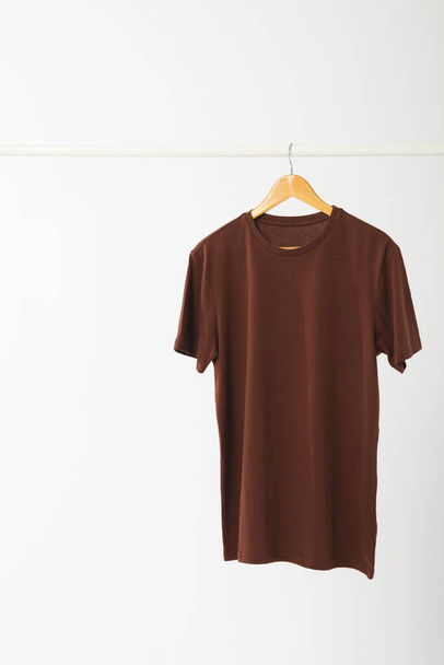 Brown t shirt on hanger hanging from clothes rail with copy space on white background. Fashion, clothes, colour and fabric concept. - Foto, Imagen