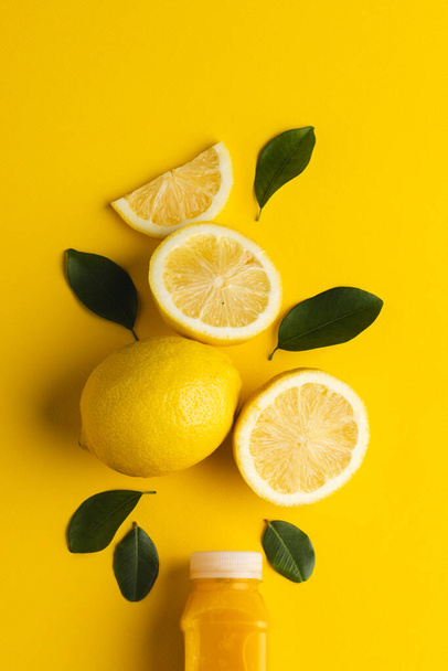 Close up of bottle with juice, lemon, lemon slices and leaves with copy space on yellow background. Fruit, food, freshness and colour concept. - 写真・画像