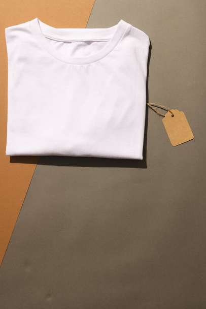 Close up of folded white t shirt with tag and copy space on brown background. Fashion, clothes, colour and fabric concept. - Fotografie, Obrázek