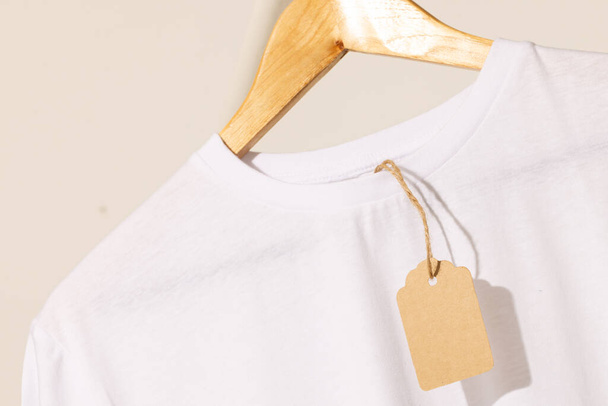 White t shirt with tag on hanger with copy space on white background. Fashion, clothes, colour and fabric concept. - Фото, зображення